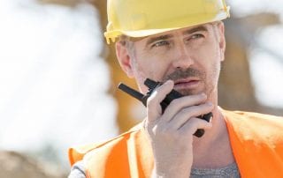 worker wearing a safety vest and hard hat using a two way radio